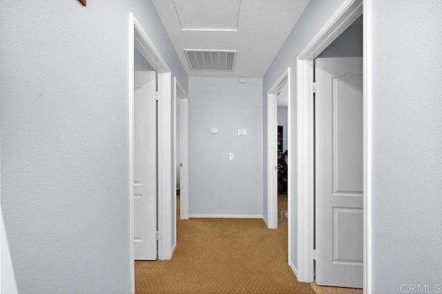 hallway featuring baseboards, visible vents, and light colored carpet