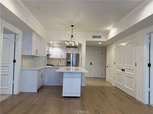 kitchen featuring under cabinet range hood, wood finished floors, visible vents, light countertops, and stainless steel refrigerator with ice dispenser