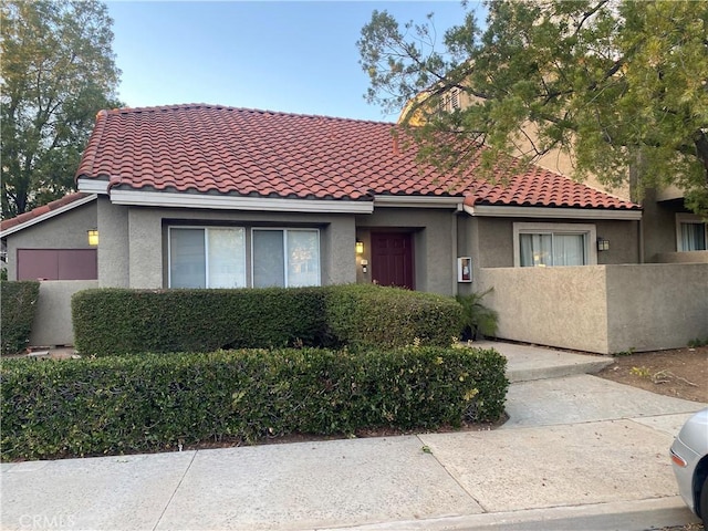 mediterranean / spanish house with a fenced front yard, a tiled roof, and stucco siding