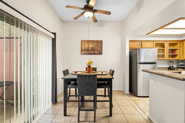 kitchen with light tile patterned floors, baseboards, glass insert cabinets, brown cabinets, and freestanding refrigerator