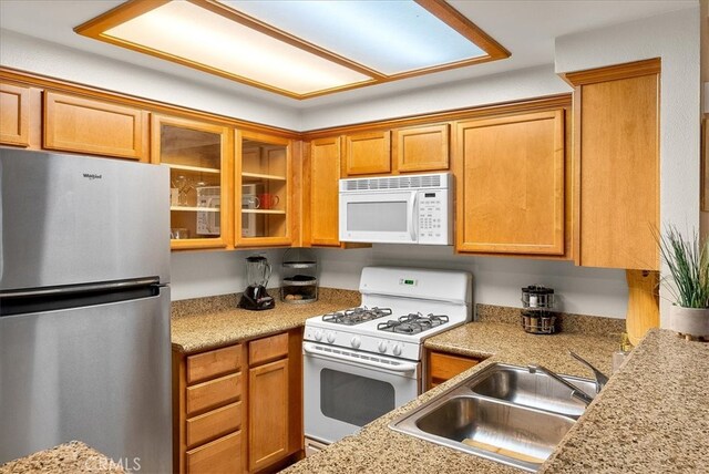 kitchen featuring white appliances, glass insert cabinets, light countertops, and a sink