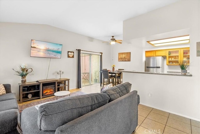 living area with light tile patterned floors, lofted ceiling, a ceiling fan, a glass covered fireplace, and baseboards