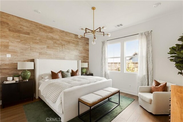 bedroom featuring an accent wall, a chandelier, wood finished floors, baseboards, and visible vents