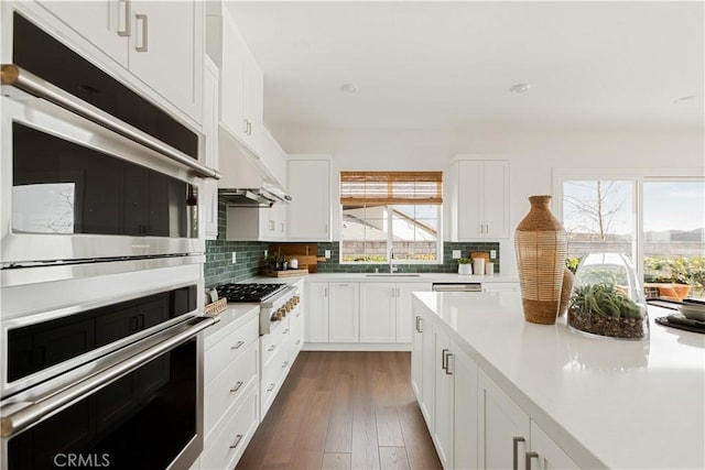 kitchen with white cabinetry, light countertops, stainless steel double oven, gas stovetop, and backsplash