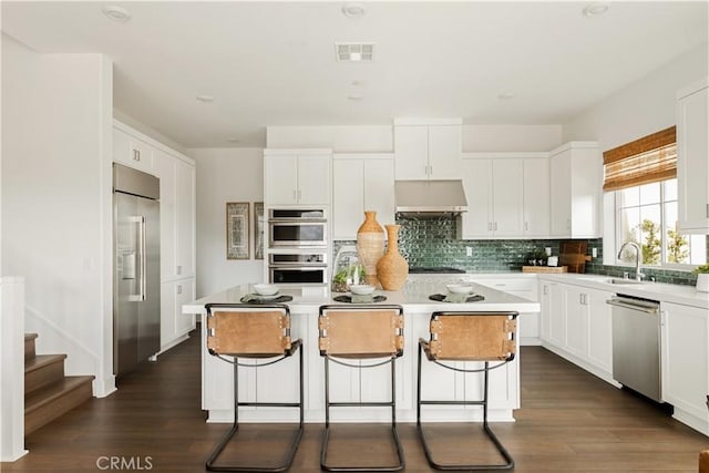 kitchen featuring a sink, backsplash, appliances with stainless steel finishes, a center island, and under cabinet range hood
