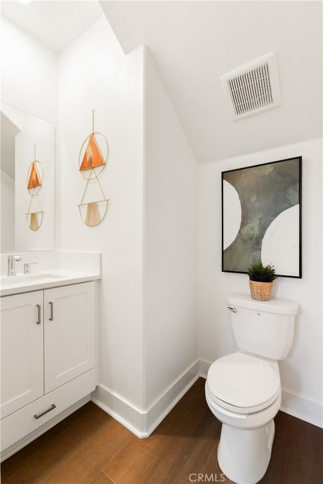 half bath with wood finished floors, vanity, baseboards, and visible vents