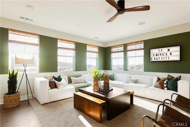living room with visible vents, light wood-type flooring, and a ceiling fan