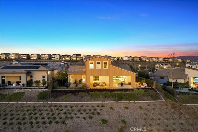 back of property at dusk with a fenced backyard, a residential view, board and batten siding, and a patio area
