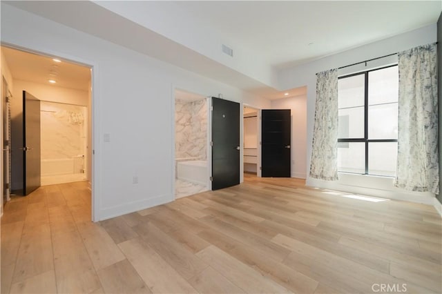 unfurnished bedroom with a walk in closet, visible vents, light wood-style flooring, ensuite bathroom, and baseboards