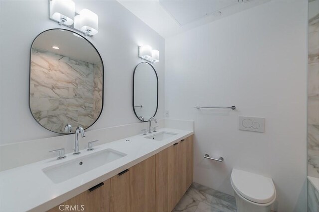 bathroom with toilet, marble finish floor, double vanity, and a sink