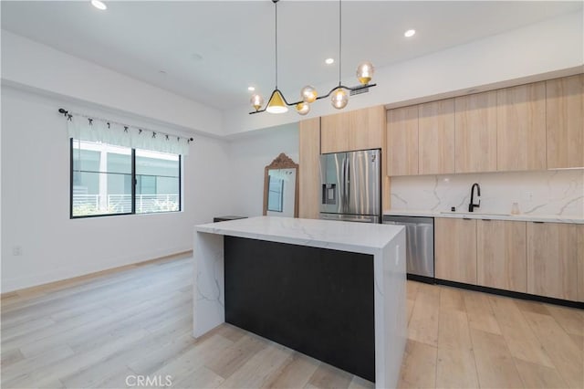 kitchen featuring modern cabinets, a kitchen island, stainless steel appliances, light brown cabinets, and a sink