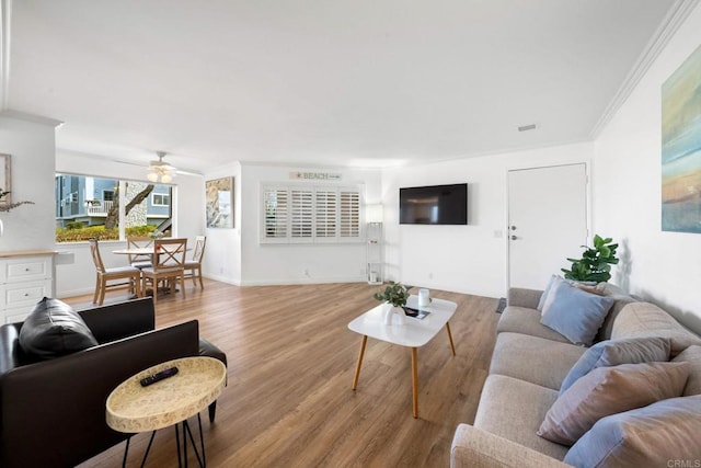 living room with visible vents, ornamental molding, a ceiling fan, light wood-type flooring, and baseboards