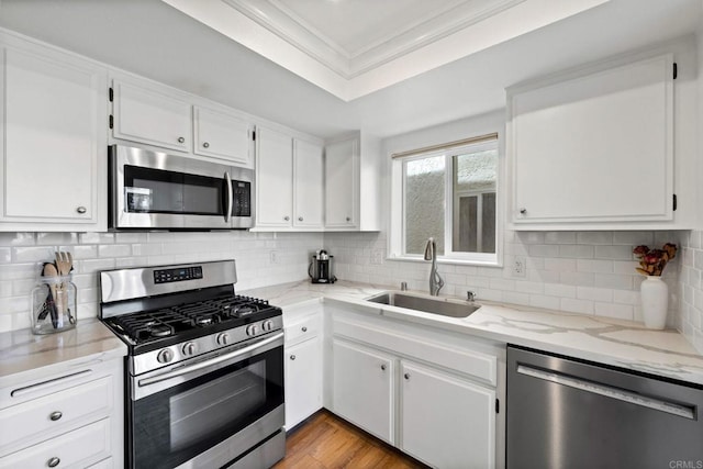 kitchen with a sink, white cabinetry, ornamental molding, appliances with stainless steel finishes, and tasteful backsplash