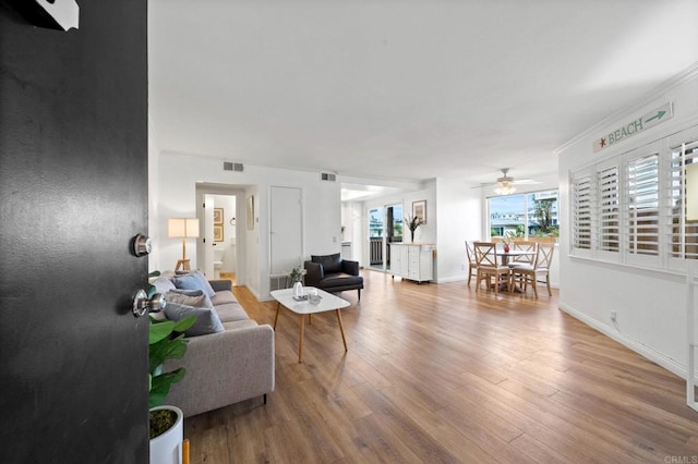 living area with a ceiling fan, visible vents, baseboards, and wood finished floors