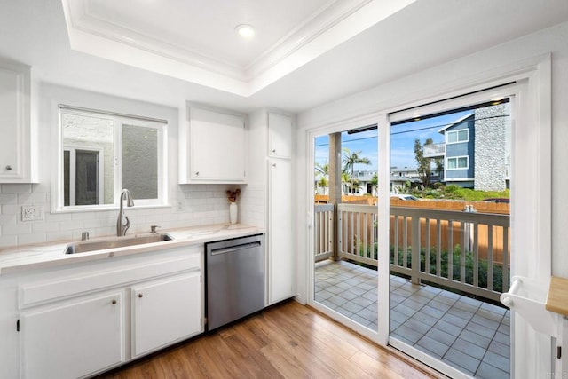 kitchen with a raised ceiling, dishwasher, a sink, light wood-style floors, and decorative backsplash