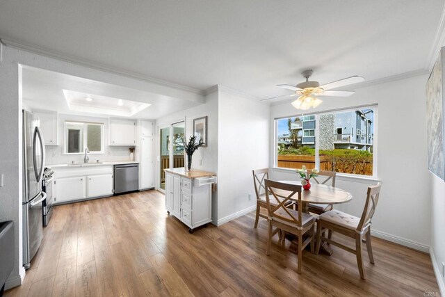dining space featuring a raised ceiling, baseboards, ornamental molding, and light wood-style flooring
