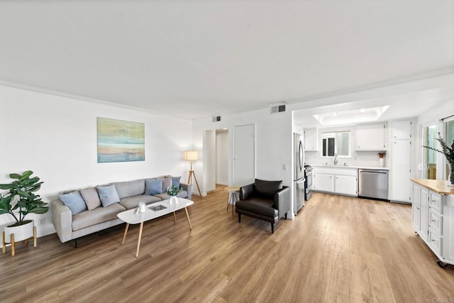 living room with light wood-style floors, visible vents, and ornamental molding