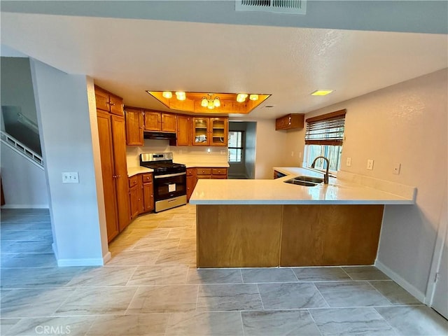 kitchen with stainless steel gas range oven, brown cabinetry, a peninsula, extractor fan, and a sink