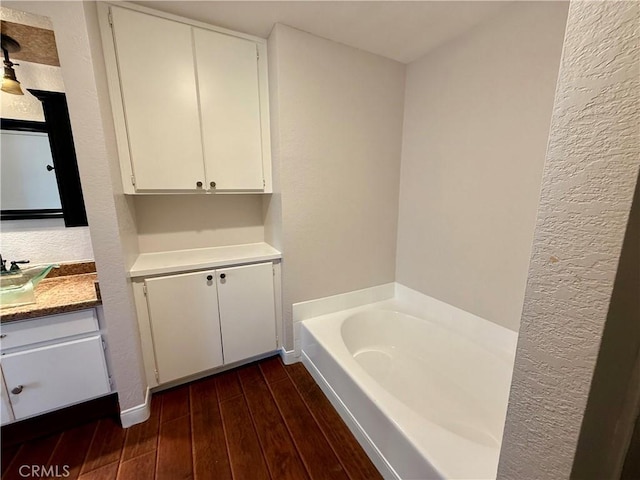 full bath with a garden tub, a textured wall, vanity, wood finished floors, and baseboards