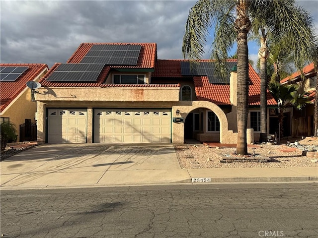 mediterranean / spanish house featuring a tile roof, stucco siding, concrete driveway, roof mounted solar panels, and a garage