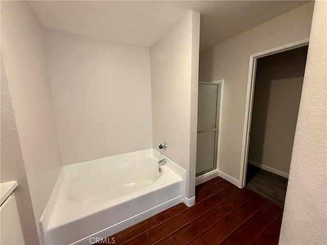 bathroom with a stall shower, a garden tub, baseboards, and wood finished floors