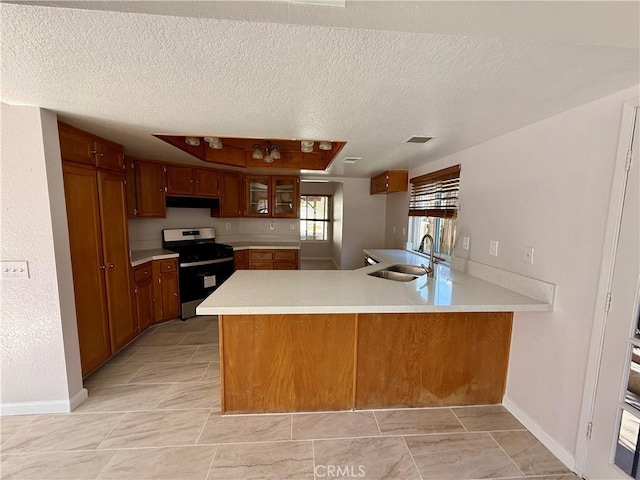 kitchen featuring stainless steel gas range oven, a peninsula, a sink, light countertops, and brown cabinets