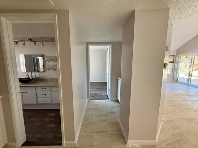 corridor featuring a textured wall, a sink, and baseboards