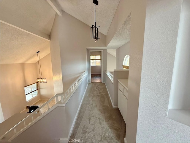 corridor featuring vaulted ceiling with beams, a textured ceiling, a chandelier, light carpet, and baseboards