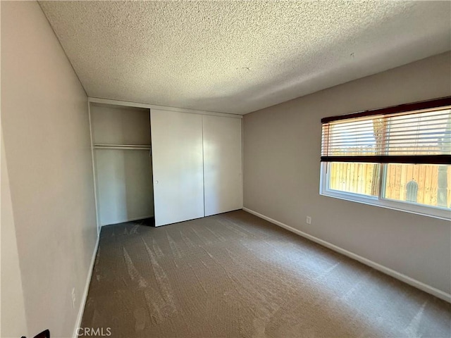 unfurnished bedroom with a textured ceiling, baseboards, dark colored carpet, and a closet