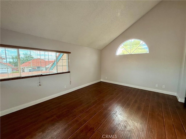 empty room featuring dark wood-style floors, vaulted ceiling, and baseboards