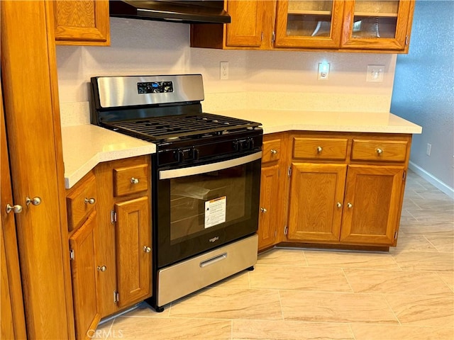 kitchen featuring brown cabinets, light countertops, glass insert cabinets, gas stove, and under cabinet range hood