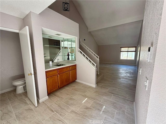 interior space with lofted ceiling, baseboards, toilet, and vanity