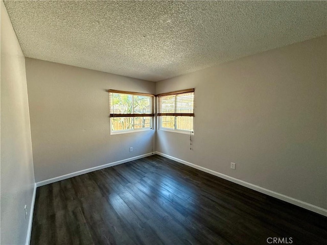 spare room with a textured ceiling, dark wood-type flooring, and baseboards