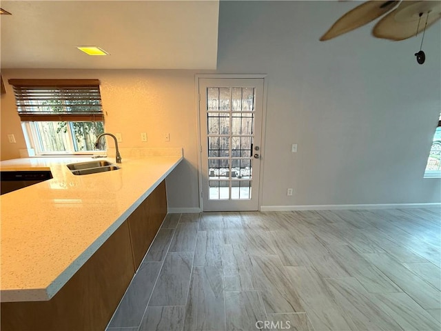 kitchen featuring ceiling fan, a sink, baseboards, stainless steel dishwasher, and light stone countertops