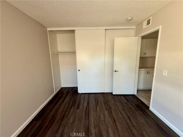 unfurnished bedroom featuring a textured ceiling, wood finished floors, visible vents, baseboards, and a closet