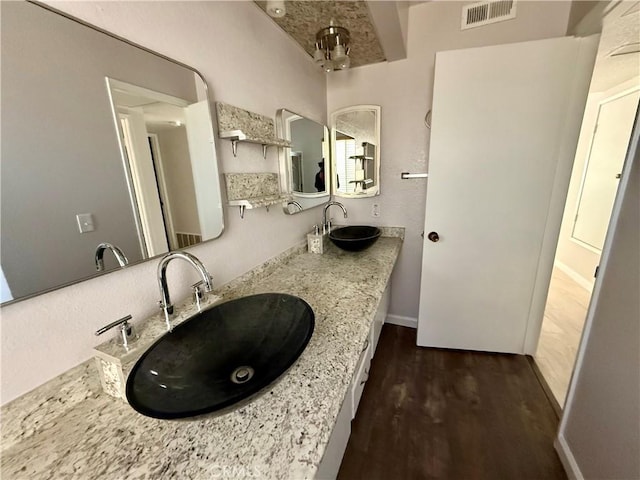 bathroom with double vanity, wood finished floors, a sink, and visible vents