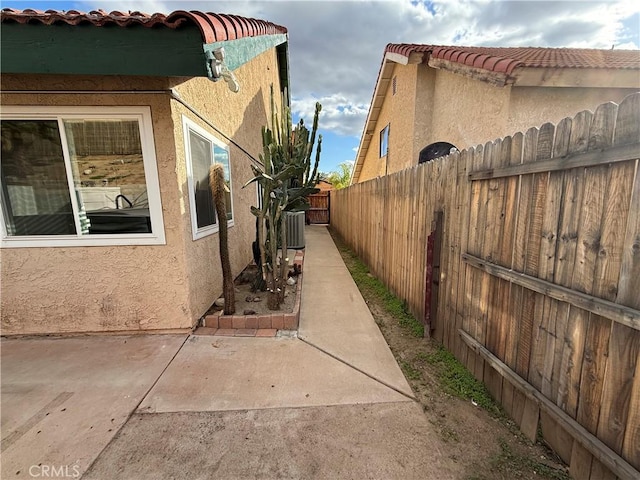 view of home's exterior featuring a tile roof, stucco siding, a patio area, fence, and central AC