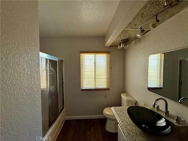 bathroom featuring toilet, wood finished floors, vanity, baseboards, and a shower with door