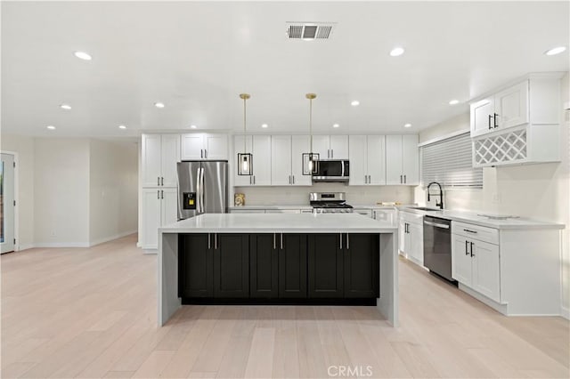 kitchen with stainless steel appliances, a spacious island, light countertops, visible vents, and a sink