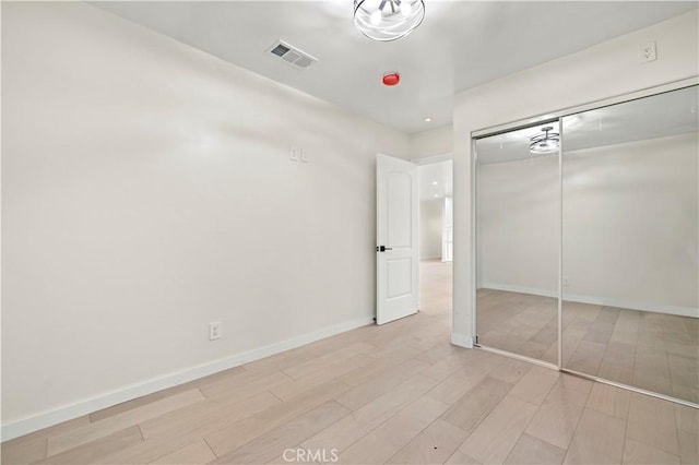 unfurnished bedroom with a closet, visible vents, light wood-style flooring, and baseboards