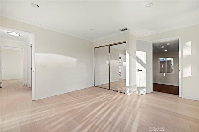 unfurnished bedroom with light wood-style flooring, visible vents, baseboards, a closet, and crown molding