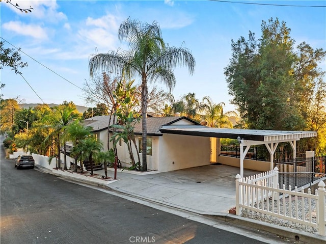 view of front of property with concrete driveway, an attached carport, fence, and stucco siding