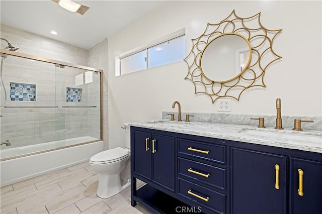 full bathroom with bath / shower combo with glass door, a sink, toilet, and double vanity