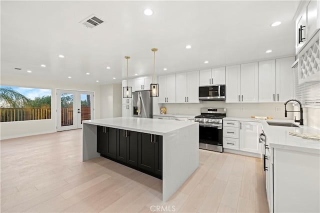 kitchen featuring light countertops, appliances with stainless steel finishes, white cabinets, a sink, and a kitchen island