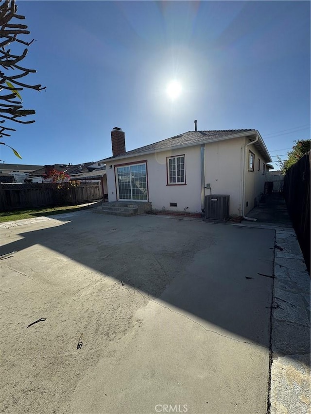 rear view of house featuring fence private yard, a chimney, central AC unit, and stucco siding