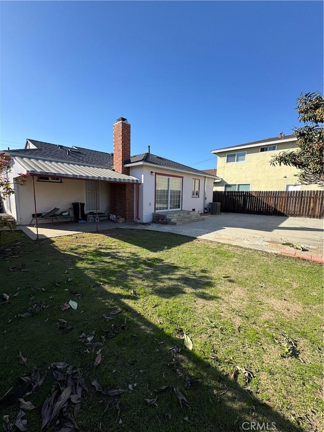 back of house featuring a patio, a chimney, fence, a yard, and stucco siding