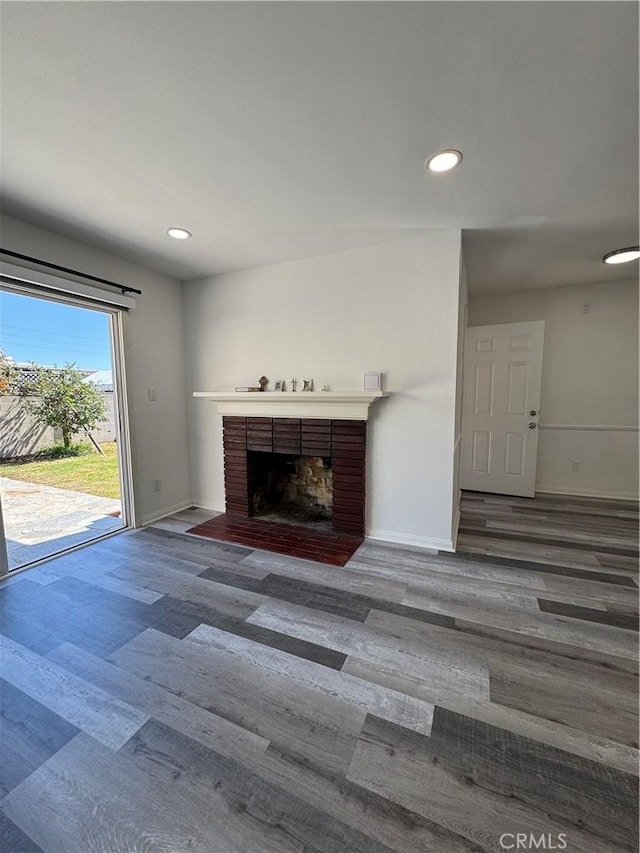 unfurnished living room featuring a brick fireplace, baseboards, wood finished floors, and recessed lighting