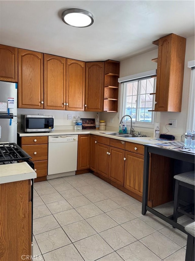 kitchen featuring white dishwasher, a sink, fridge, brown cabinets, and stainless steel microwave