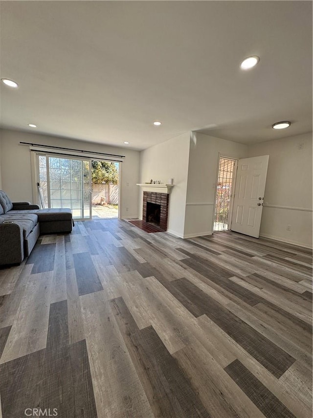 unfurnished living room with a brick fireplace, baseboards, wood finished floors, and recessed lighting