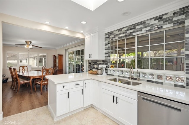 kitchen with crown molding, light countertops, backsplash, stainless steel dishwasher, and a sink